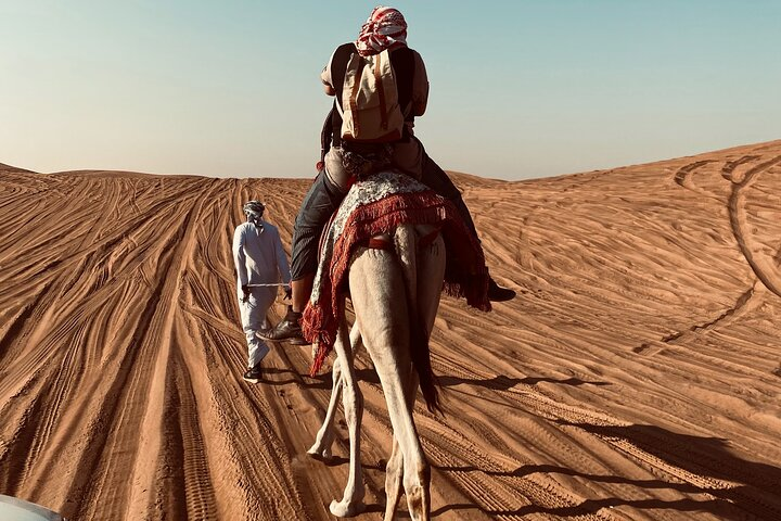 Experience the serene beauty of the desert at dusk riding a camel across the golden sands while a gentle breeze enhances your journey through this stunning landscape.